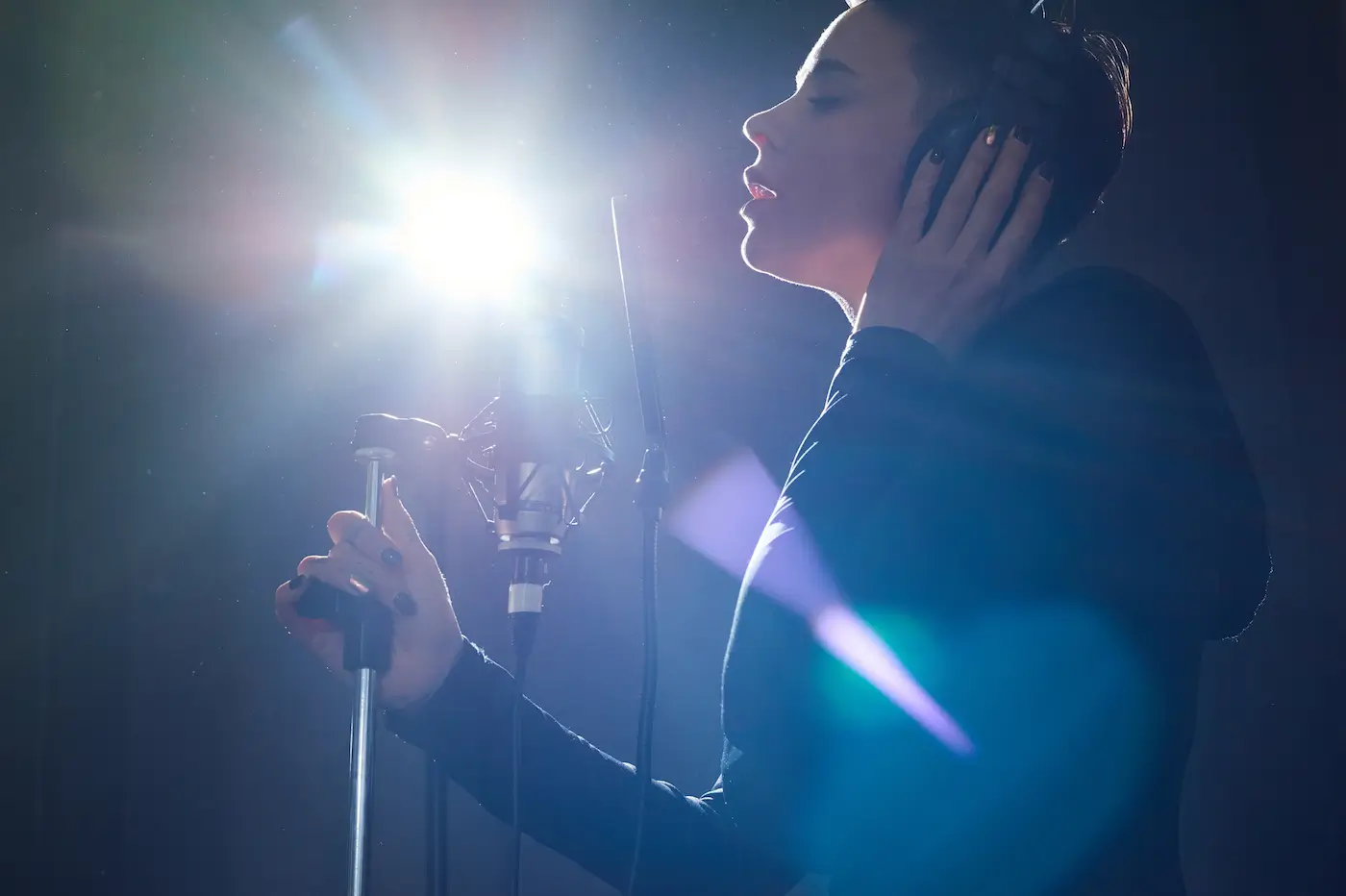 A singer wearing headphones sings into a microphone in a dim studio with bright light shining, capturing the passion behind Taylor Swift's songs.