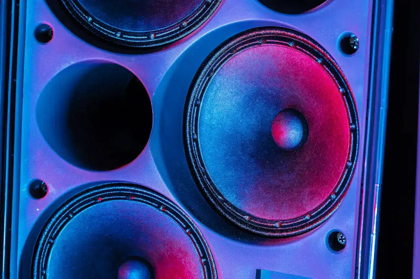 Close-up of a vibrant speaker cone glowing in blue and pink light, showing the power and clarity of professional music production equipment.