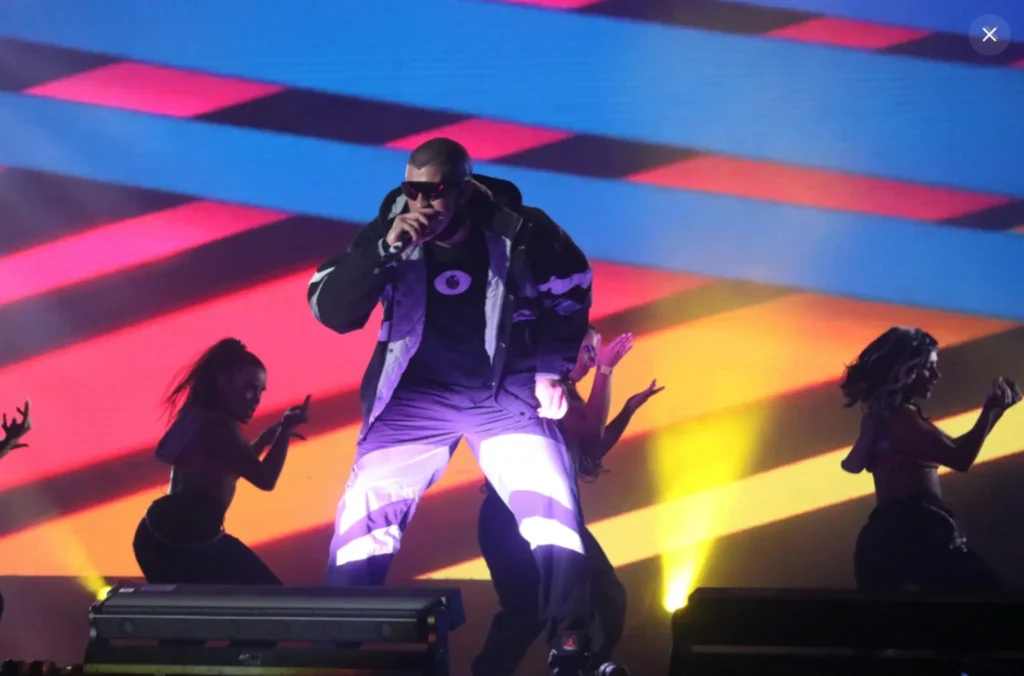 Singer performs on stage with dancers and colourful lights during a Bad Bunny Grammy performance.